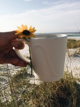 yellow flower and coffee mug on a beach 