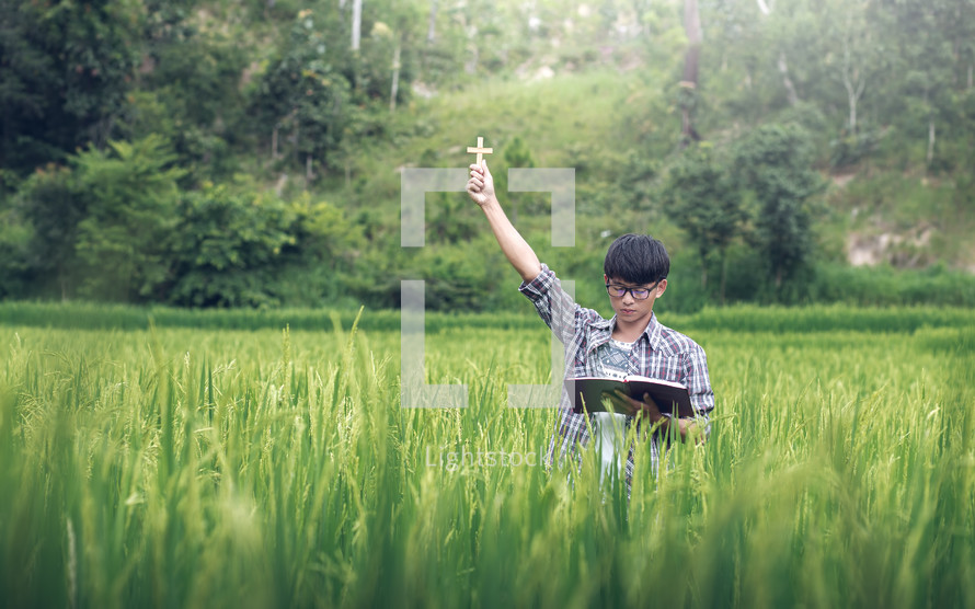 A young man in a rice field with raised hand praying 