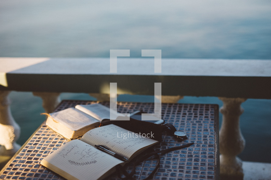open Bible, journal, pen, phone, and watch on a table outdoors 