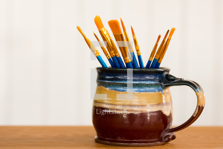 a blue mug of paint brushes with a white background