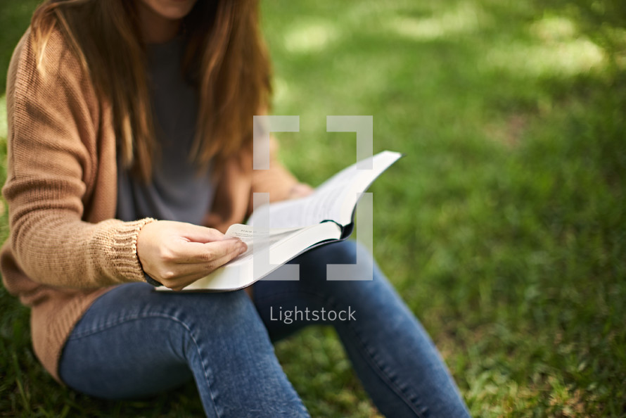 a woman sitting in the grass reading a Bible 
