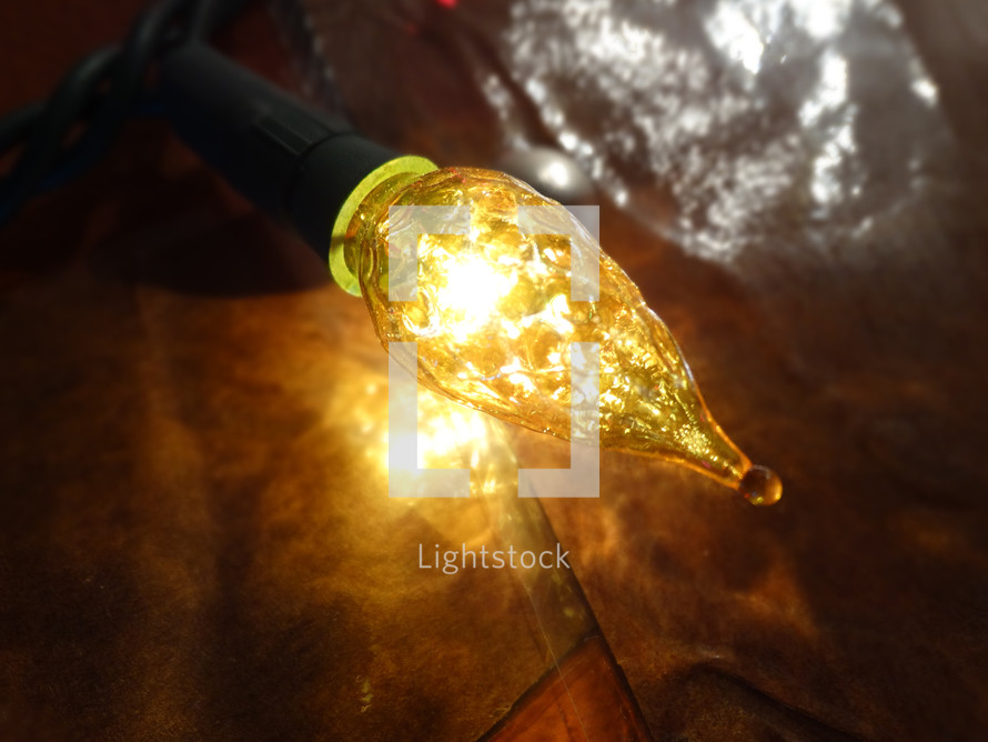 Close up of large yellow tree light bulb with reflections against dark wall