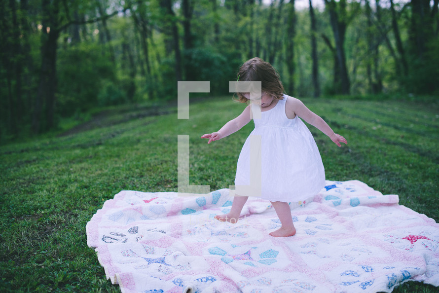little girl dancing on a blanket in the grass