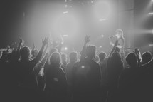 Silhouette of an audience with raised hands worshiping at a concert.