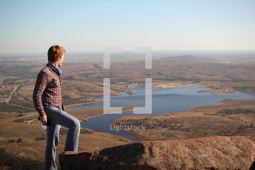 a man standing at the top of a mountain looking out at a lake 
