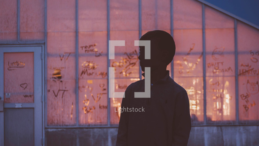 silhouette of a boy standing in front of an old warehouse building 