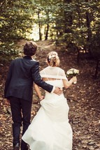 bride and groom walking down a path in a forest 