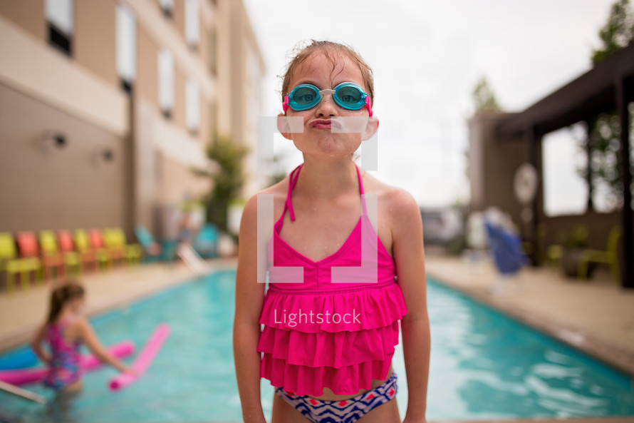 girl making a silly face standing in front of a swimming pool 