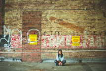 a woman sitting on the ground in front of a graffiti covered wall 