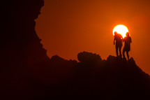 silhouettes of women standing on a mountain at sunset 