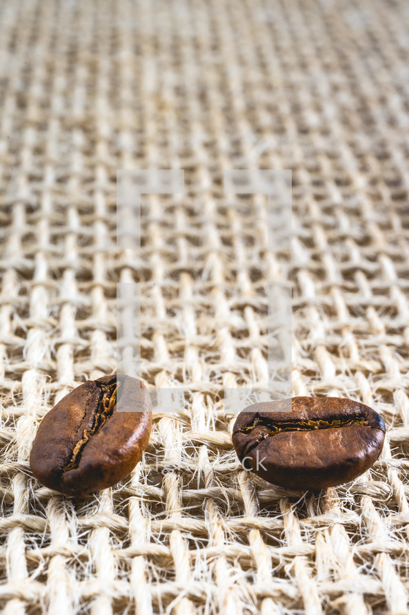 Close up from a few coffee beans laying down on a Burlap fabric background. Background voor coffee related products.
