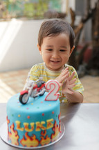 Happy Asian toddler boy clapping his hands after blowing out the candle on his cake. Shot outdoors.