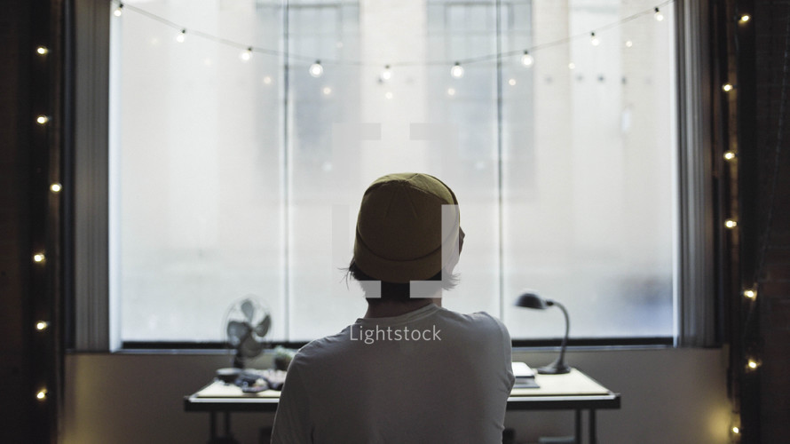 man at a desk looking out a window in an apartment 