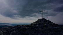 A single wooden cross on a rocky hill under dark skies.