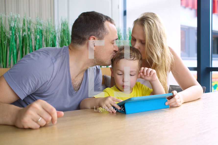 Parents kissing son playing on ipad