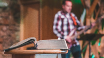 open Bible on a pulpit and worship team playing music 