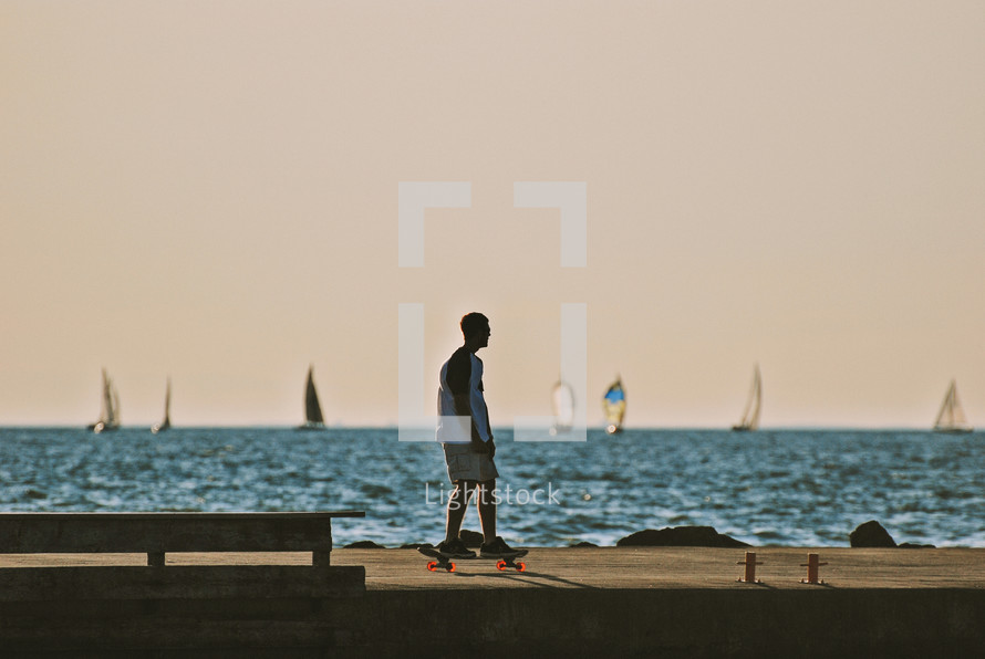 man on a skateboard on a dock and sailboats 
