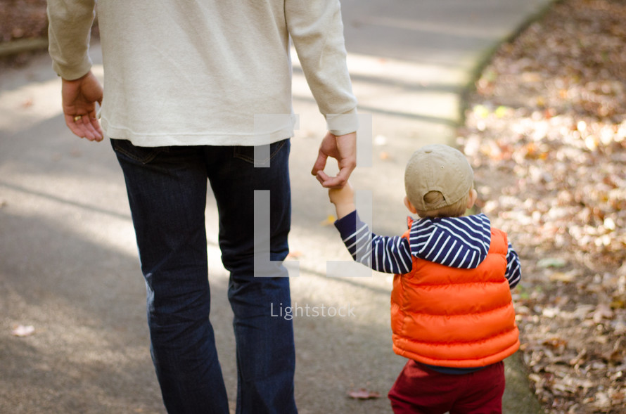 a father walking holding hands with his toddler son 