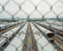 view of trains in a train yard through chain link fence 