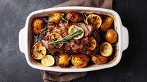 Easter. Roasted Lamb with potatoes and rosemary in baking dish on dark background, top view