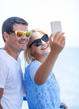 Cheerful couple in sunglasses taking mobile selfie