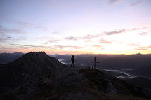 cross and silhouette of a man on a mountain top at sunset 