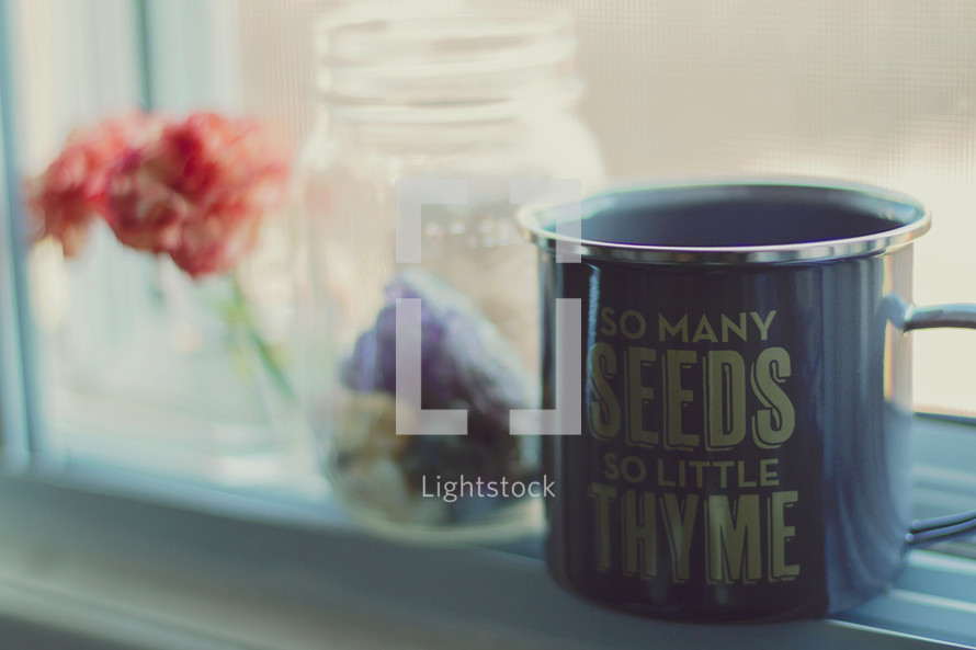 Cleverly worded coffee mug on a windowsill beside a geranium and Mason jar.