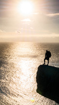 silhouette of a man with a backpack on the edge of a sea cliff at sunset 