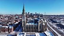 Aerial view of a snow-covered cathedral-style church in St. Louis, Missouri in the wintertime with the arch and downtown in the background.