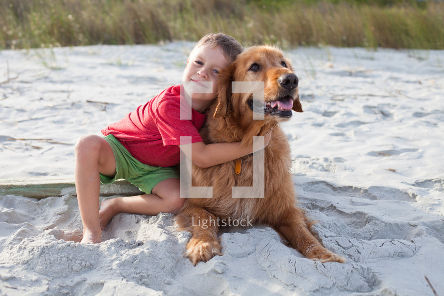 boy child hugging a dog on the beach