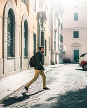 a man with a backpack walking across a cobblestone street 