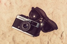 a camera and sunglasses in sand 
