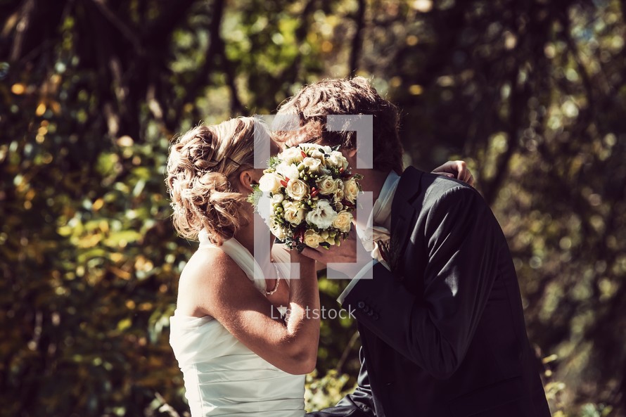 A bride and groom kiss behind the bridal bouquet.