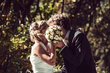 A bride and groom kiss behind the bridal bouquet.