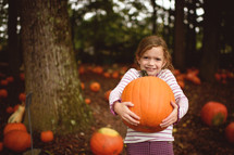 a girl child holding a pumpkin in a pumpkin patch 