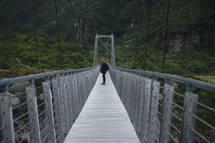 a woman walking across a swinging bridge 