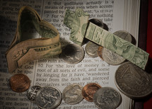 Paper money heart and cross with coins on pages of Bible open to 1 Timothy 6:10 -- "for the love of money."