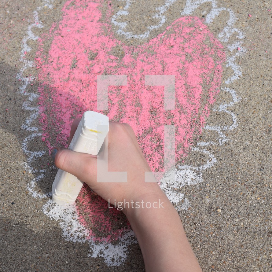 a child drawing a Valentine's heart on concrete with sidewalk chalk 