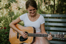 a young woman sitting on a bench playing a guitar 