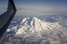 a plane wing flying over a snow capped mountain 