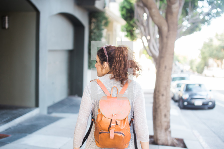 A young woman walking along a street wearing a backpack.