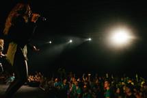 A singer on stage singing to a crowd of young people.