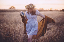 a woman with flowers in her hair walking through a field holding a camera 