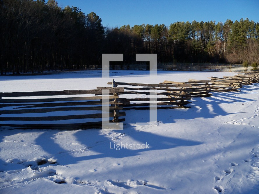 A wooden fence cascades across the landscape covered by fresh snow on a winter day in Virginia.