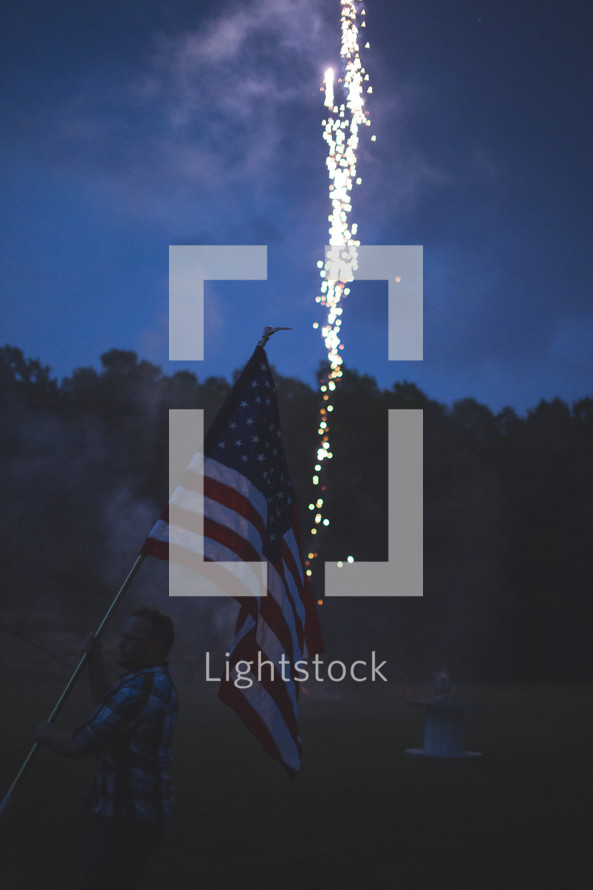 man holding an American flag in front of fireworks 