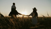 Silhouette of a friendly family of farmers walking in a wheat field at sunset. Father holding on his shoulders son. Family playing enjoying sunset in wheat field on summer. Sunset on a wheat field.