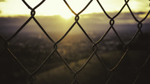 Sunrise through a chain link fence.