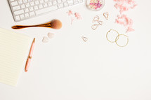 Women working space with make up blush, pink flowers, earrings over white background. 