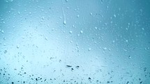 Close up view of water drops falling on glass. Rain running down on window. Rainy season, autumn. Raindrops trickle down, blue sky
