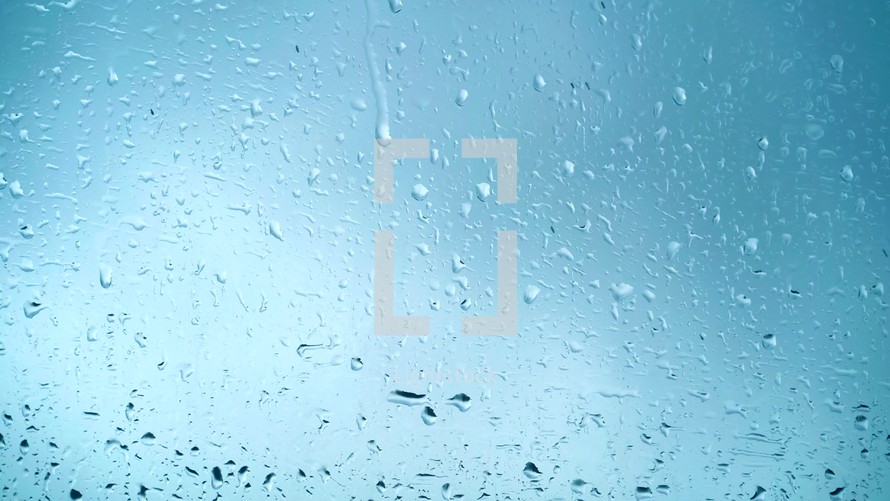 Close up view of water drops falling on glass. Rain running down on window. Rainy season, autumn. Raindrops trickle down, blue sky
